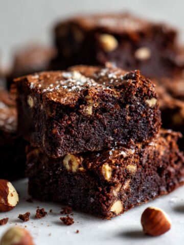 Overhead shot of homemade hazelnut brownies recipe with chopped hazelnuts on a white kitchen counter, cut into rustic squares with crumbs scattered.