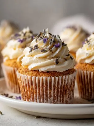 Homemade honey lavender cupcakes recipe with rustic frosting swirls and lavender buds on a white kitchen counter, shot from above.