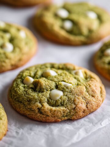 Overhead photo of homemade matcha white chocolate cookies recipe with melted chips on parchment paper, shot on a white kitchen counter.