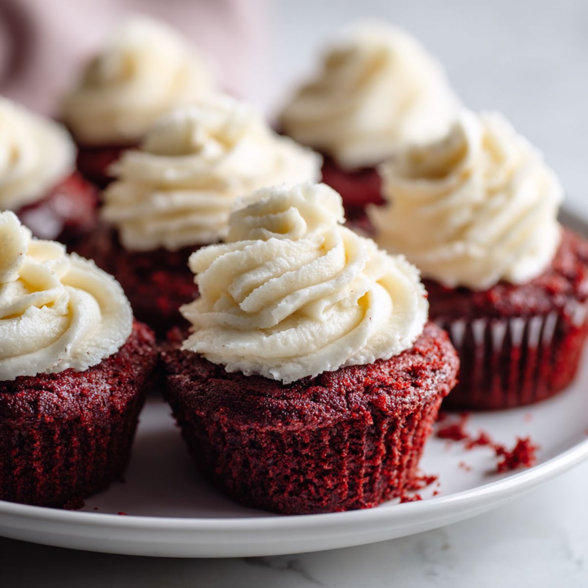 Overhead photo of homemade mini red velvet cupcakes recipe with cream cheese frosting on a white kitchen counter.