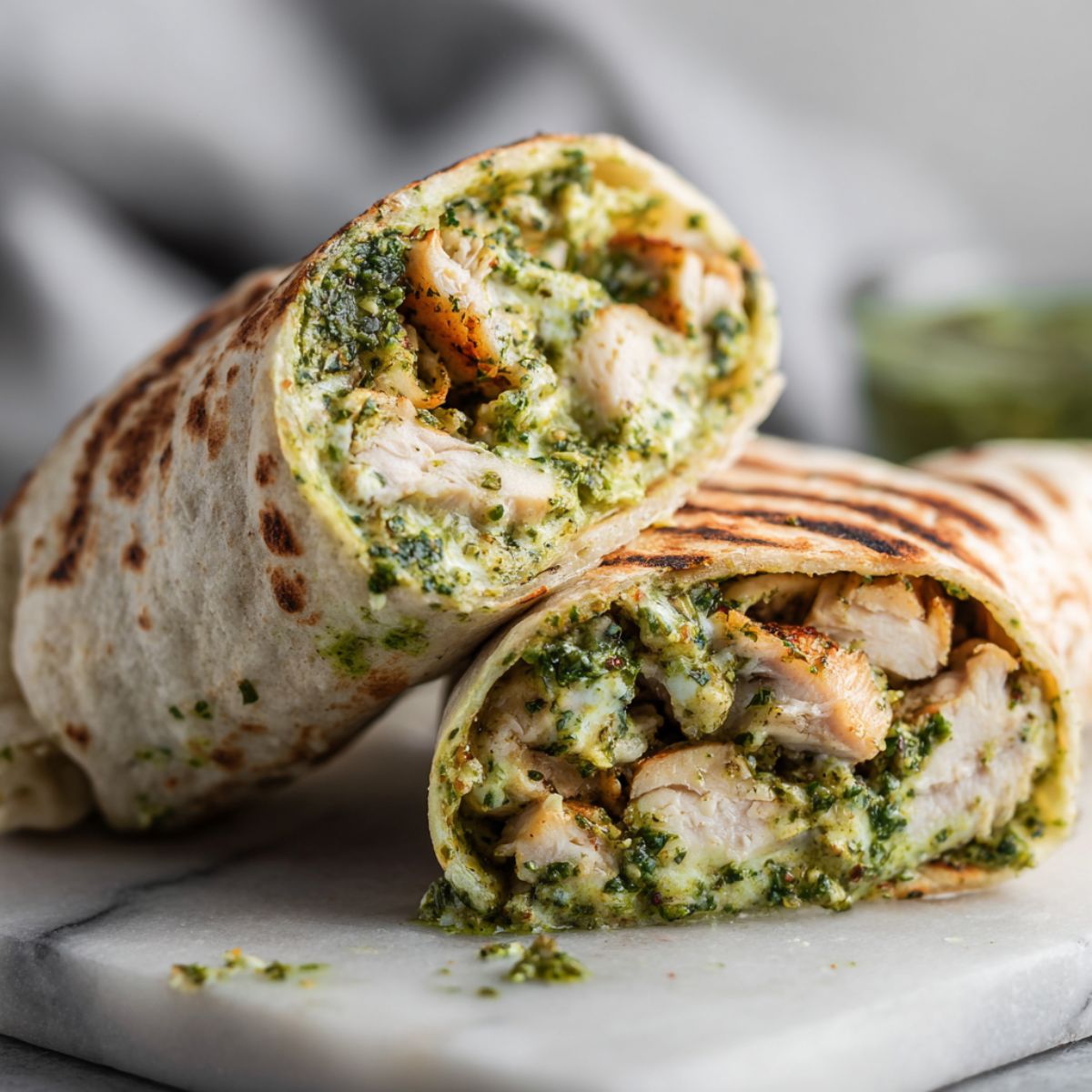 Overhead homemade pesto chicken wrap recipe cut in half on a white marble counter with crumbs and pesto smudges, casual kitchen look.