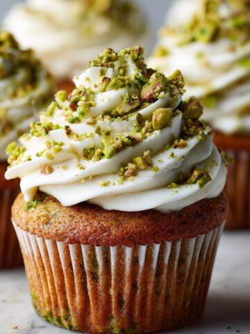 Homemade pistachio cupcakes recipe with imperfect frosting and crushed pistachios on a white marble kitchen counter, photographed from above.