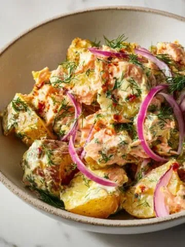 Homemade smoked salmon potato recipe served in a rustic bowl with dill and onions on a white marble kitchen counter.