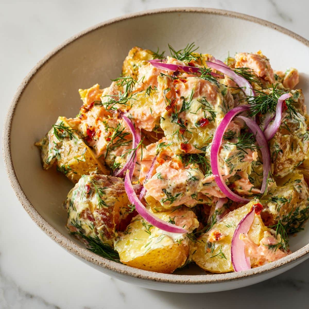 Homemade smoked salmon potato recipe served in a rustic bowl with dill and onions on a white marble kitchen counter.
