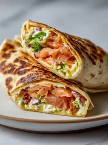 Homemade smoked salmon wraps recipe cut in half on a white plate with cream cheese, avocado, and dill, shot from above on a white kitchen counter