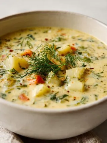 Homemade creamy dill pickle soup recipe in a white ceramic bowl, topped with fresh dill on a white kitchen counter.
