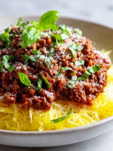 Overhead photo of spaghetti squash bolognese recipe served on a plate with parmesan and basil on a white kitchen counter, homemade style.