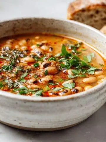 Homemade spicy black eyed pea soup recipe served in a ceramic bowl on a white kitchen counter, shot from above in a cozy and rustic style.