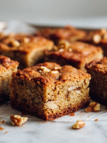 Overhead view of homemade walnut blondies recipe cut into squares on a white marble kitchen counter with crumbs scattered.