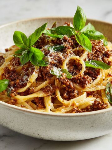 Homemade walnut bolognese recipe pasta served in a white bowl on a marble kitchen counter, shot from above with a natural, homemade look.