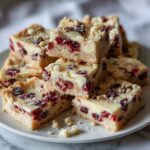 Homemade white chocolate cranberry bars recipe cut into rustic squares on a white kitchen counter with crumbs scattered.