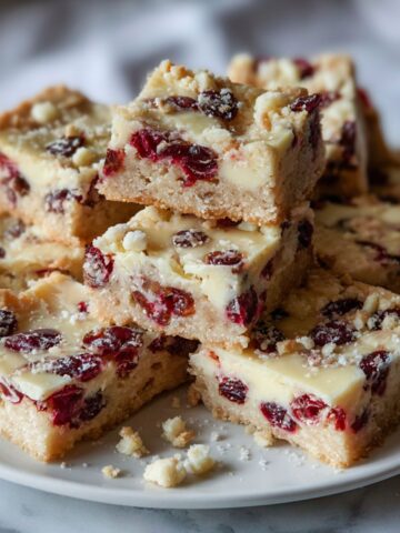 Homemade white chocolate cranberry bars recipe cut into rustic squares on a white kitchen counter with crumbs scattered.