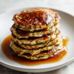 Overhead view of homemade zucchini bread pancakes recipe stacked on a white kitchen counter with syrup and berries, imperfectly rustic and cozy.