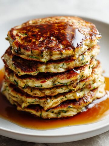 Overhead view of homemade zucchini bread pancakes recipe stacked on a white kitchen counter with syrup and berries, imperfectly rustic and cozy.