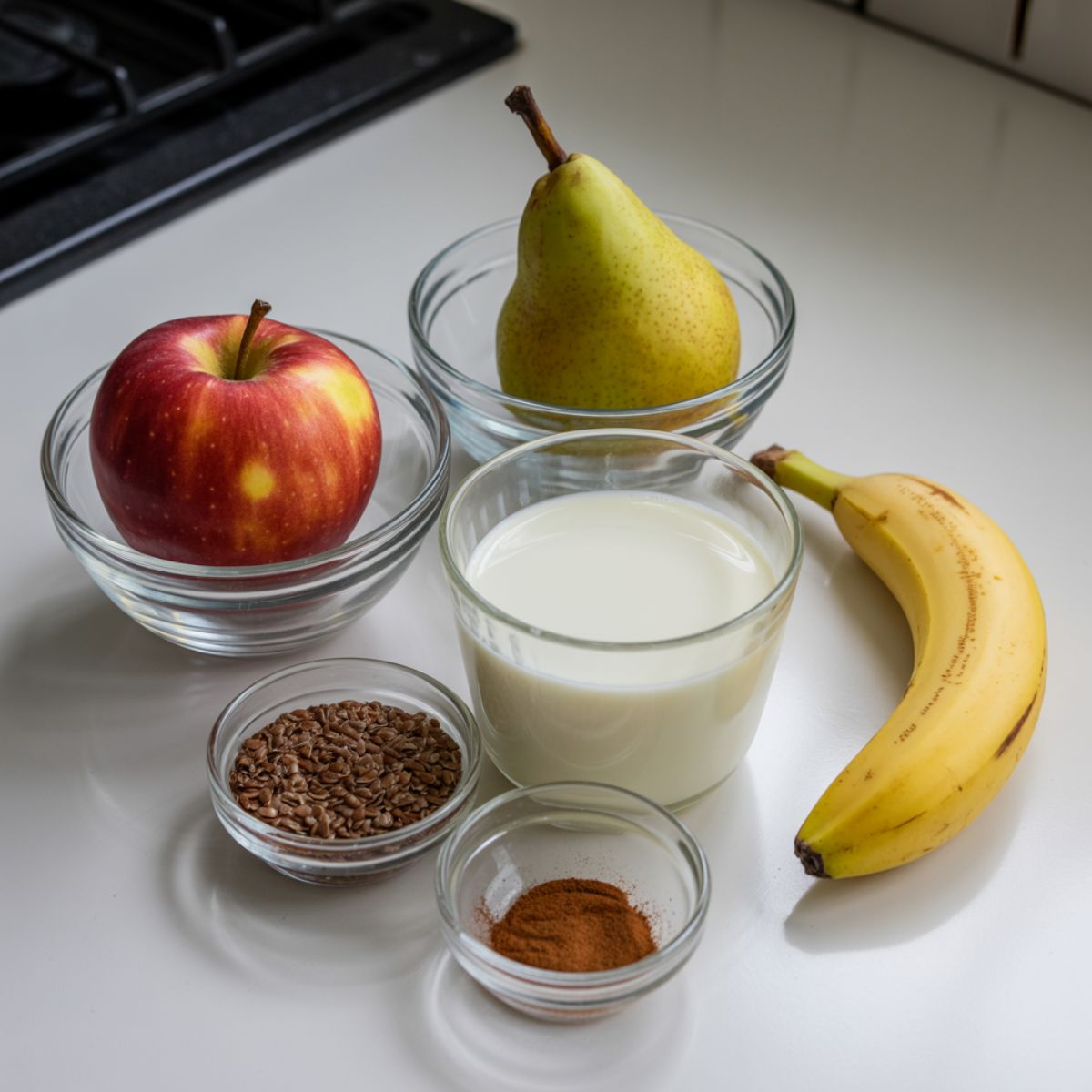 Flat lay of fresh apple, pear, banana, almond milk, flaxseeds, and cinnamon on a white kitchen counter for making apple pear smoothie