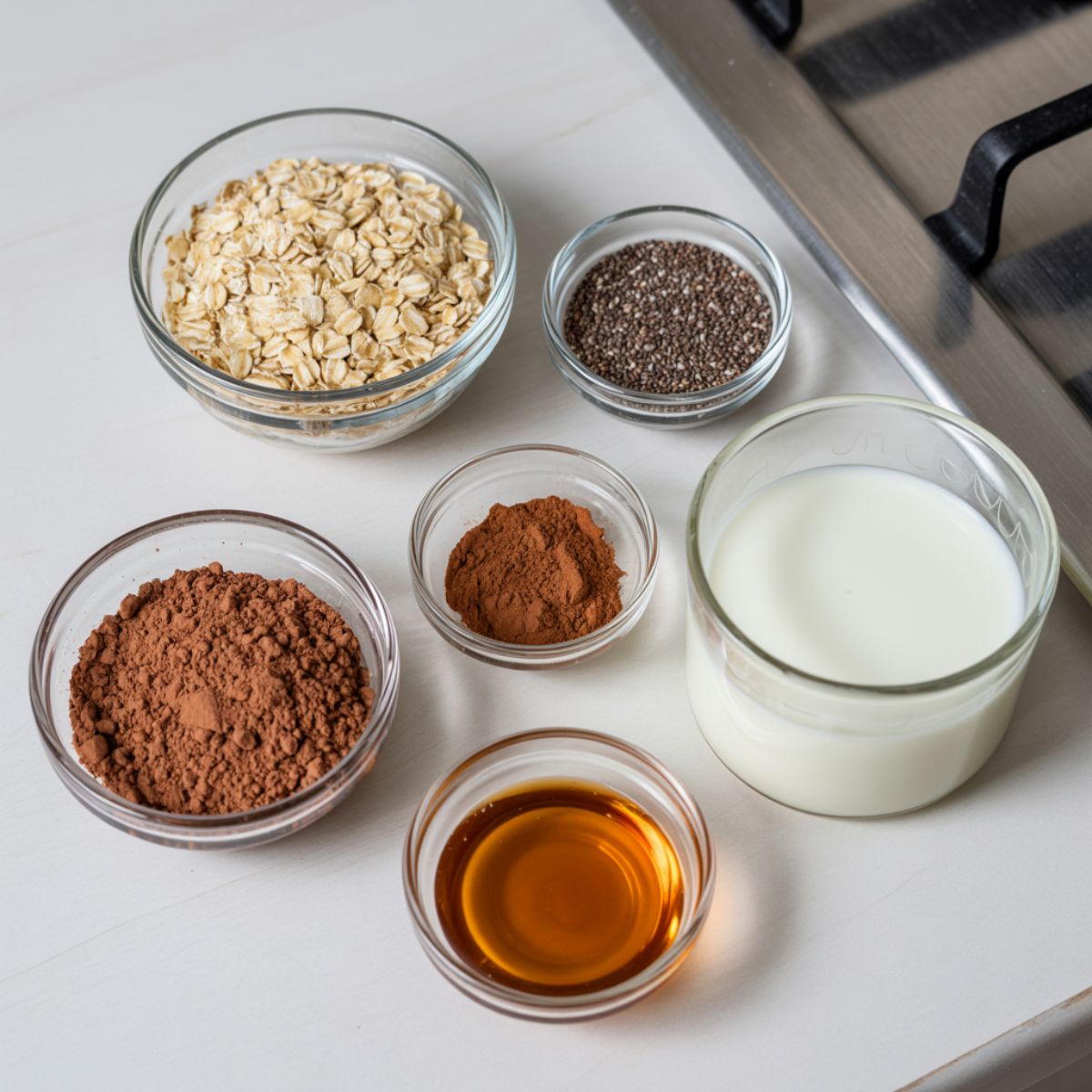 Flat lay of mocha overnight oats ingredients including oats, cocoa powder, instant coffee, milk, chia seeds, and maple syrup on a white kitchen counter