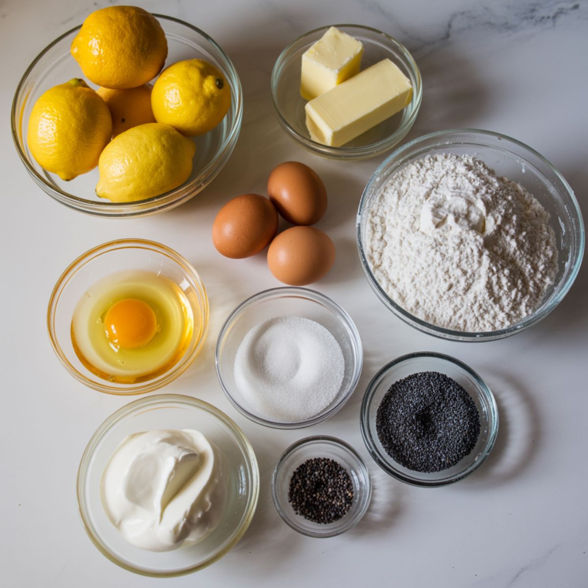 Overhead shot of ingredients for lemon poppy seed pound cake on white kitchen counter with fresh lemons and poppy seeds.