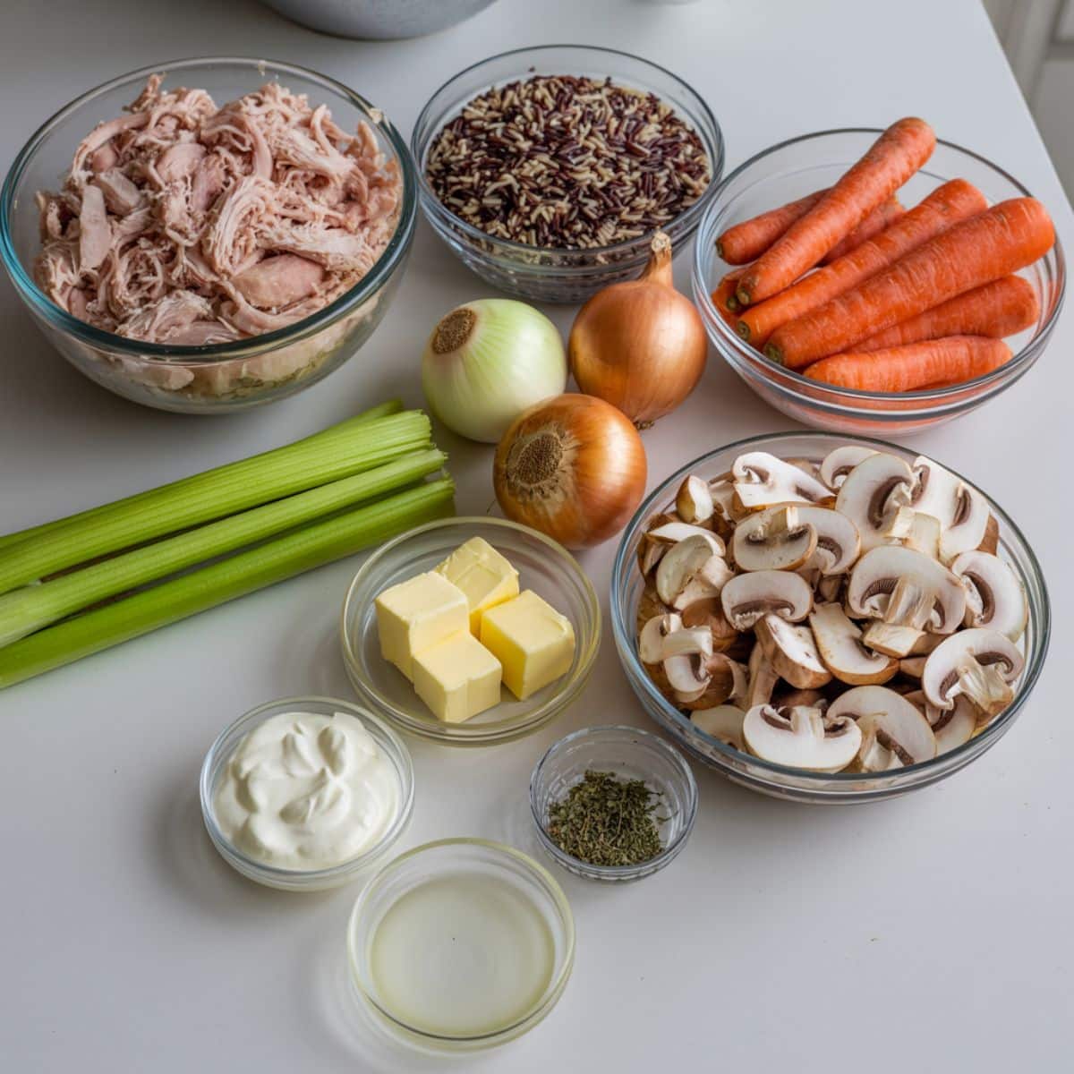 Overhead view of turkey wild rice soup ingredients on a white kitchen counter, including shredded turkey, wild rice, vegetables, butter, cream, and herbs.