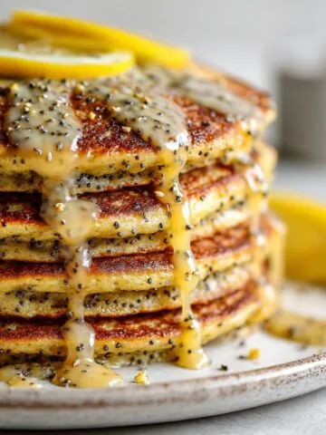 Stack of fluffy lemon poppy seed pancakes recipe drizzled with lemon glaze on a white kitchen counter, photographed from above in a homemade style.