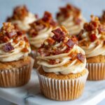 Homemade maple bacon cupcakes recipe topped with candied bacon and maple buttercream frosting on a white marble counter, photographed from above.