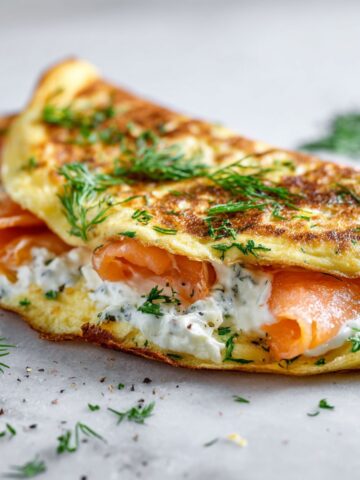 Overhead shot of a homemade smoked salmon omelette recipe folded with salmon and dill on a white kitchen counter.