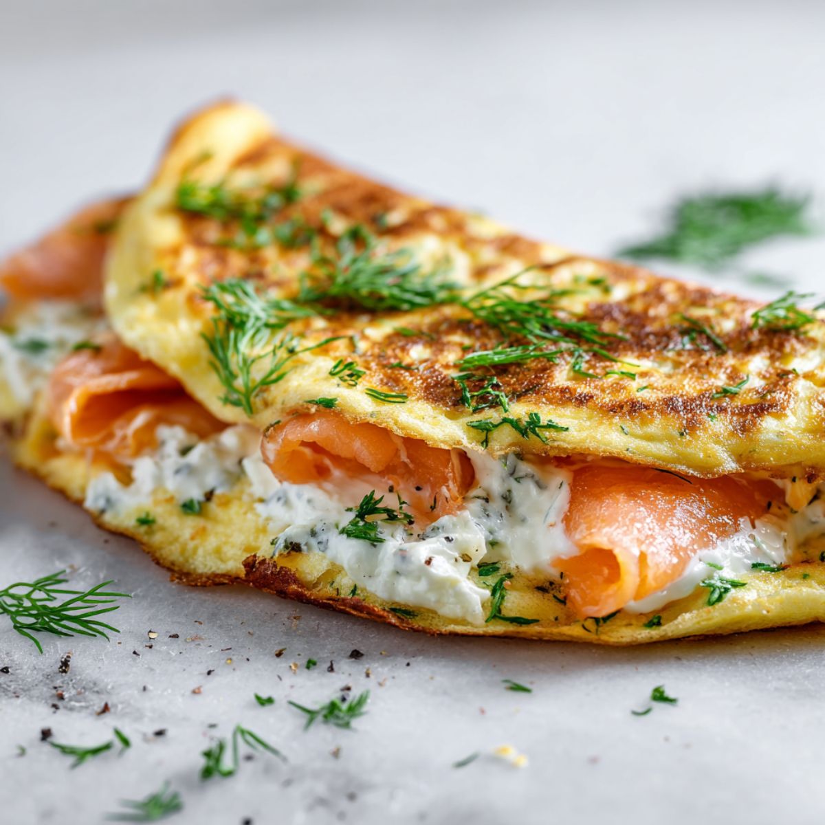 Overhead shot of a homemade smoked salmon omelette recipe folded with salmon and dill on a white kitchen counter.