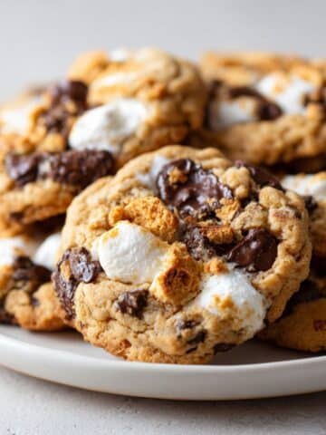 Homemade s’mores cookies recipe with melted chocolate, marshmallows, and graham cracker pieces on a white kitchen counter, photographed from above.
