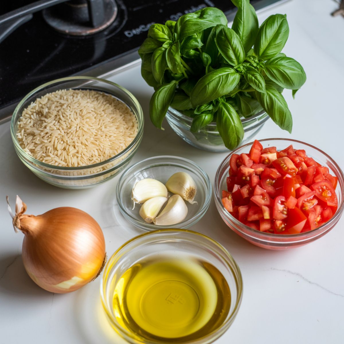 Overhead photo of tomato basil rice ingredients on a white kitchen counter including rice, basil, tomatoes, garlic, onion, and olive oil.