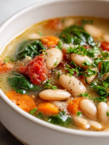 Rustic homemade Tuscan white bean soup recipe in a white bowl on a white marble counter, overhead shot with fresh herbs on top.