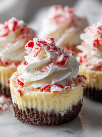 Homemade candy cane cheesecake bites recipe topped with whipped cream and crushed candy canes on a white marble kitchen counter, photographed from above for a cozy Christmas dessert feel.