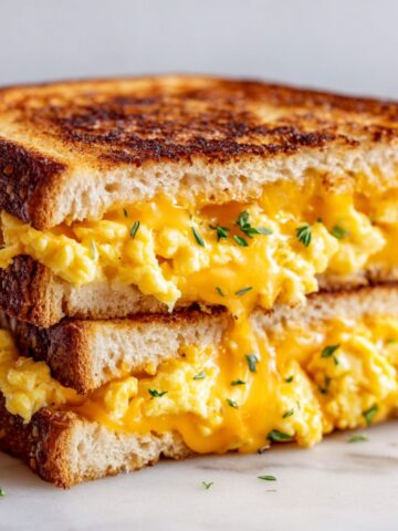 Homemade cheese breakfast sandwich recipe on white kitchen counter, sliced in half to show melted cheddar and fluffy eggs.