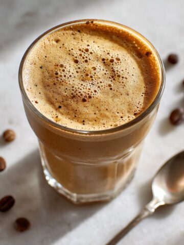 Homemade espresso smoothie recipe in a clear glass jar with frothy top on a white marble counter, photographed from above with a cozy natural morning light.