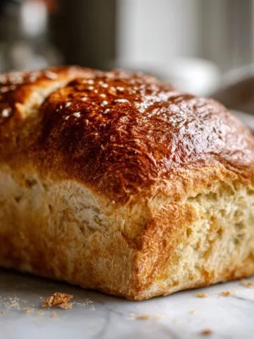 Golden homemade honey bread recipe loaf on a white kitchen counter with crumbs, photographed from above in a real home kitchen.