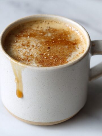 Homemade honey almond milk flat white recipe served in a white ceramic mug on a white marble counter with honey drizzle, photographed from overhead in natural morning light.