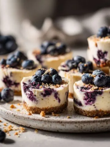Homemade blueberry cheesecake bites recipe on a white kitchen counter, imperfectly arranged on a plate with crumbs showing a real handmade dessert feel.