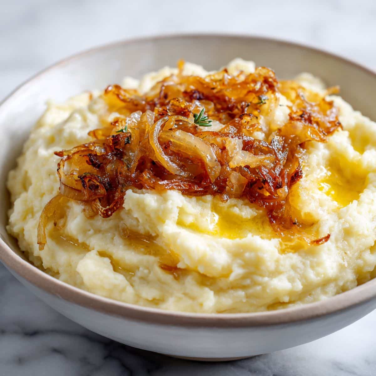 Overhead view of creamy caramelized onion mashed potatoes recipe topped with golden onions and melting butter on a white kitchen counter.