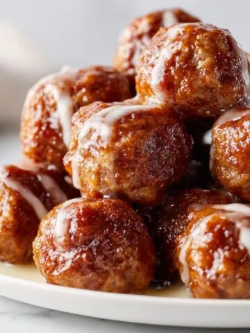 Overhead shot of homemade meatball bites recipe on a white marble kitchen counter with glaze drips, looking real and imperfect.