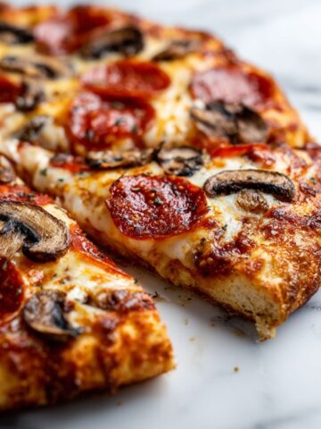Overhead shot of a freshly baked homemade pepperoni and mushroom pizza recipe on a white marble counter with imperfect slices and melted cheese.