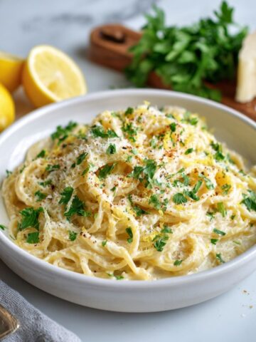 Overhead view of creamy lemon parmesan recipe pasta on a white kitchen counter, sprinkled with parsley and lemon zest in a cozy homemade setting.
