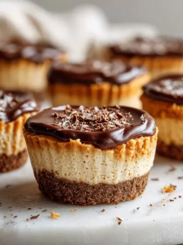 Overhead photo of homemade peanut butter cheesecake bites recipe with chocolate ganache on a white kitchen counter, looking real and slightly imperfect.