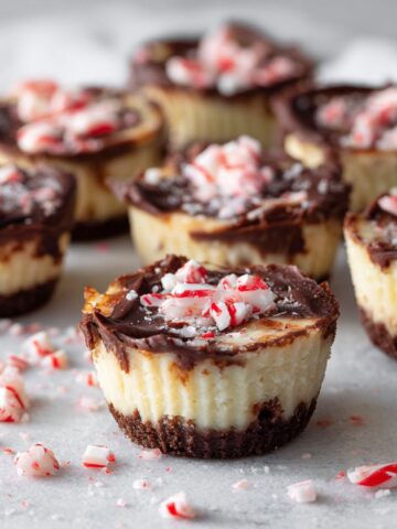 Overhead view of homemade peppermint cheesecake bites recipe on a white kitchen counter, topped with crushed candy canes and chocolate, looking cozy and imperfectly made.