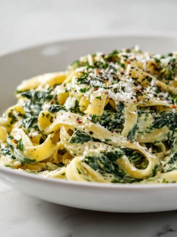 Overhead shot of creamy spinach tagliatelle recipe pasta on a white plate with parmesan, homemade and imperfectly plated on a marble counter.