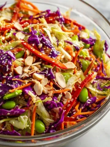Homemade Asian sesame salad recipe with cabbage, carrots, bell pepper, edamame, and sesame seeds on a white kitchen counter, overhead shot.