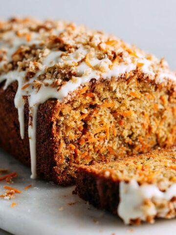 Homemade carrot cake bread recipe loaf with cream cheese glaze, sliced on a white marble kitchen counter in a casual homemade style.