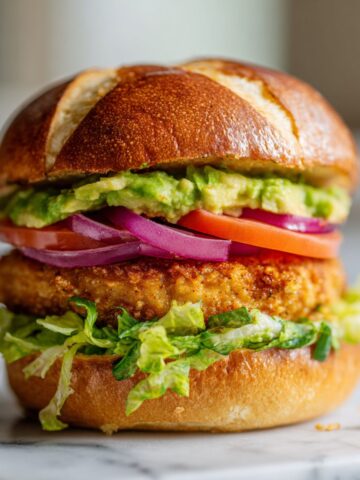 Overhead view of a homemade chicken avocado burger recipe on a white marble counter with tomato, lettuce, and mashed avocado, looking juicy and freshly made.