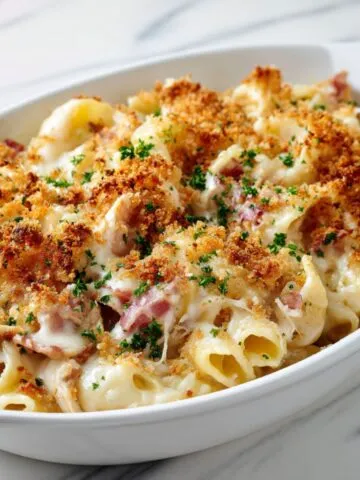Homemade chicken cordon bleu pasta recipe with creamy Swiss sauce, ham, and golden breadcrumbs on a white kitchen counter.