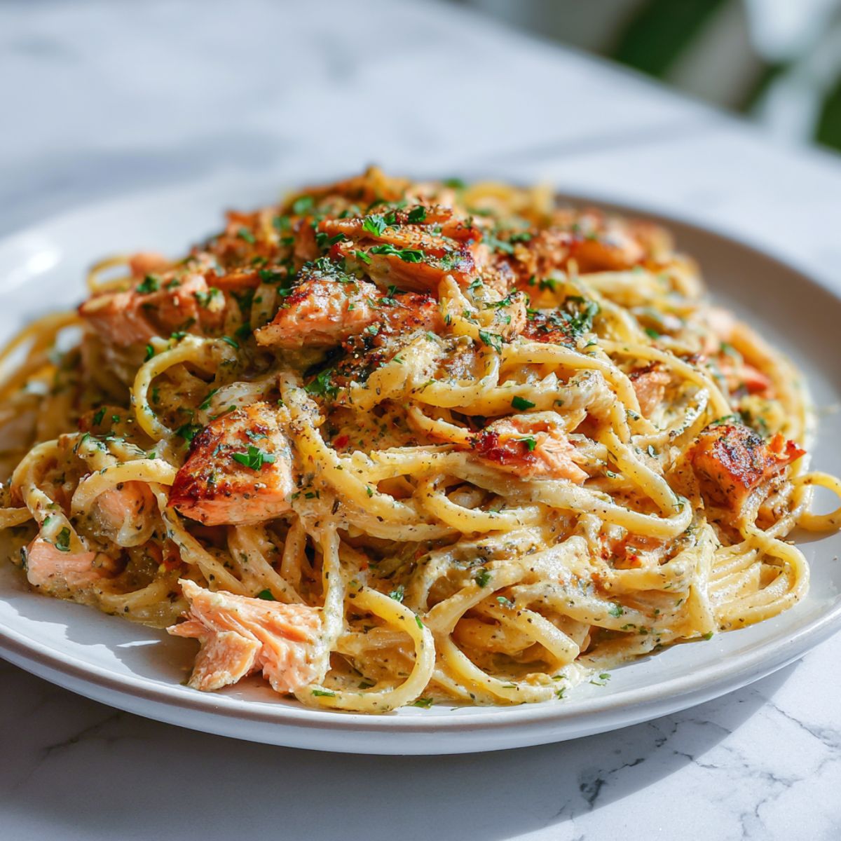 Homemade creamy Cajun salmon pasta recipe topped with seared salmon flakes and parsley, shot from above on a white kitchen counter.