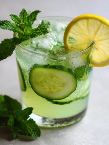 Fresh homemade cucumber mint juice recipe served in a glass with ice, lemon slices, and mint leaves on a white kitchen counter, overhead angle.