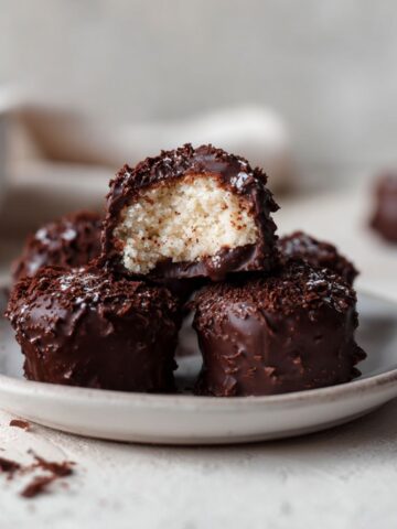 Overhead view of homemade chocolate covered cheesecake bites recipe on a white counter, dipped in glossy chocolate with a natural homemade look.