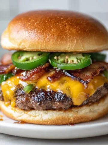 Homemade jalapeño burger recipe with melted cheddar, bacon, and fresh jalapeño slices on a white kitchen counter — photographed from above in a real home kitchen.